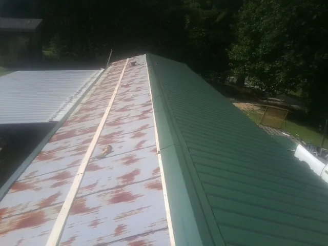 Old rusted panels beside newly installed green metal roofing — Wind Damage Roof Repair by Roofing Brothers in Greenville