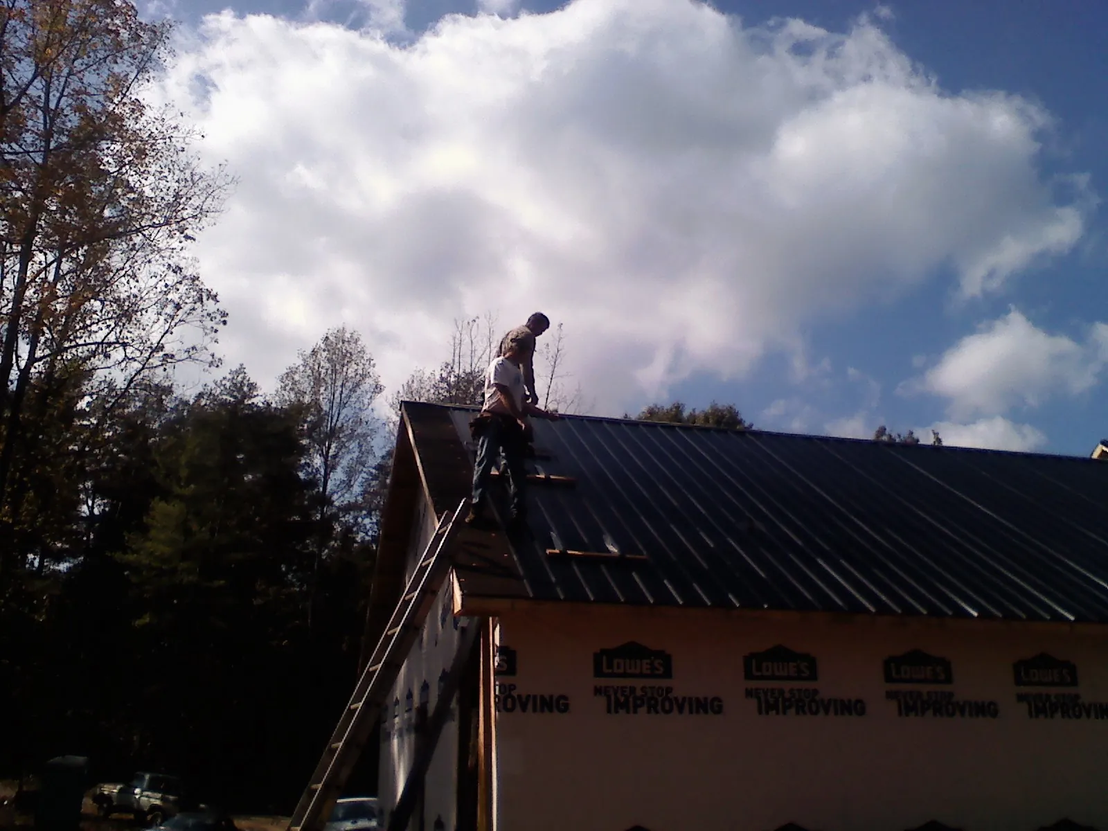 Roofer fastening dark metal panels high against a cloudy sky, from a Roof Inspection job in Greenville